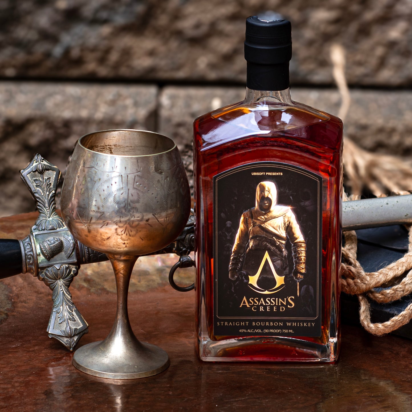 A bottle of Assassin's Creed Straight Bourbon Whiskey is in front of a saber and sitting next to the chalice.